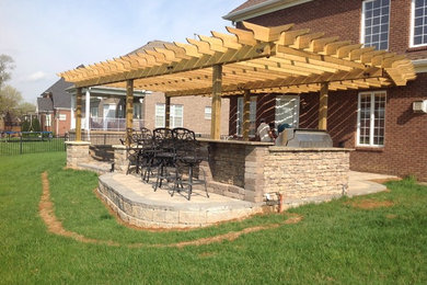 Cette photo montre une grande terrasse arrière chic avec une cuisine d'été, des pavés en béton et une pergola.