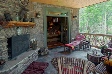 Immagine di un ampio patio o portico american style nel cortile laterale con un focolare, pavimentazioni in pietra naturale e un tetto a sbalzo