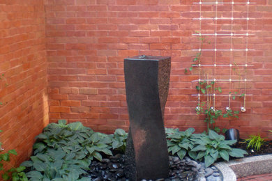 Imagen de patio contemporáneo pequeño en patio con fuente y adoquines de ladrillo