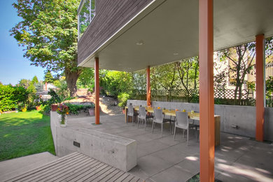 Immagine di un grande patio o portico design dietro casa con lastre di cemento e un tetto a sbalzo