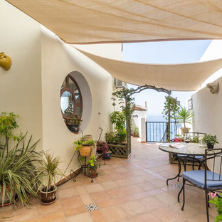 Ejemplo de patio mediterráneo con jardín de macetas, suelo de baldosas y toldo