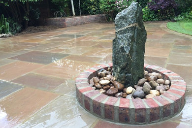 Large classic back patio in Cambridgeshire with a water feature, natural stone paving and no cover.
