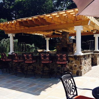 Large elegant backyard stone patio kitchen photo in New York with a pergola