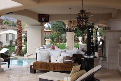 Large classic back patio in Phoenix with a fire feature, natural stone paving and a roof extension.