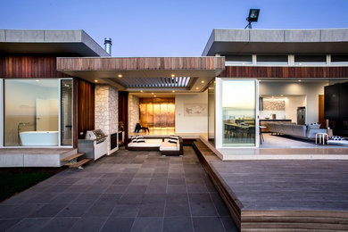 Cette image montre une grande terrasse minimaliste avec une cuisine d'été, une cour, des pavés en béton et un auvent.