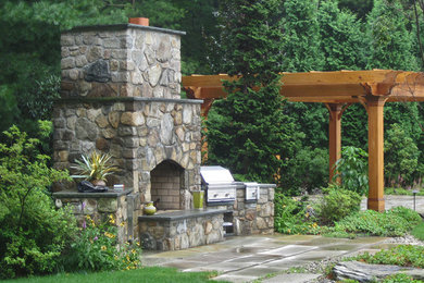 This is an example of a large classic back patio in Boston with a fire feature, natural stone paving and a pergola.