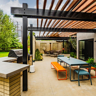 Réalisation d'une grande terrasse latérale vintage avec une cheminée, une dalle de béton et une pergola.