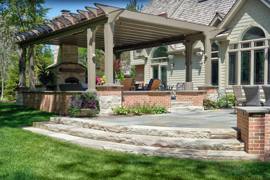 Example of a large cottage backyard stone patio design in Chicago with a fireplace and a pergola
