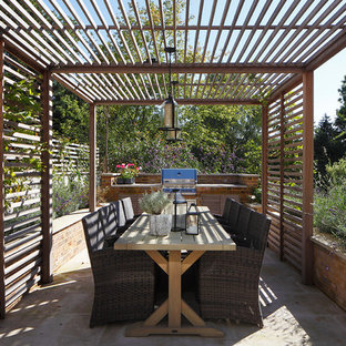 This is an example of a traditional back patio in London with an outdoor kitchen, concrete paving and a pergola.