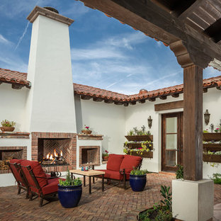 Immagine di un patio o portico mediterraneo in cortile con pavimentazioni in mattoni, nessuna copertura e un caminetto