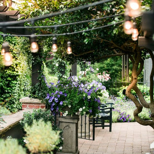 Cette photo montre une terrasse avec des plantes en pots arrière chic de taille moyenne avec des pavés en brique et une pergola.