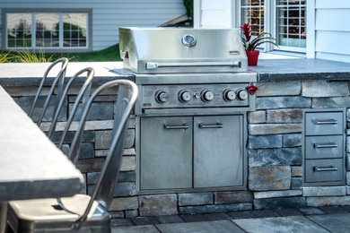 Patio kitchen - large traditional backyard stone patio kitchen idea in New York