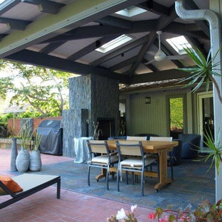 Immagine di un grande patio o portico etnico dietro casa con un focolare, piastrelle e un tetto a sbalzo