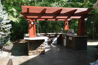 This is an example of a medium sized classic back patio in Grand Rapids with an outdoor kitchen, a pergola and natural stone paving.