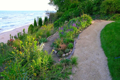 Expansive eclectic sloped xeriscape partial sun garden for summer in Chicago with a retaining wall and gravel.