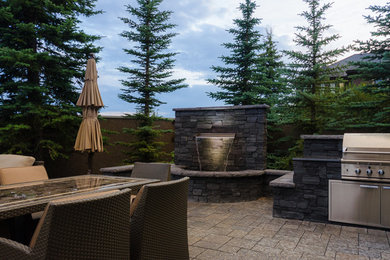 Large transitional backyard stone patio kitchen photo in Calgary with no cover