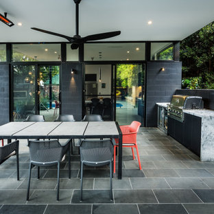 Large contemporary backyard patio in Melbourne with an outdoor kitchen, natural stone pavers and an awning.
