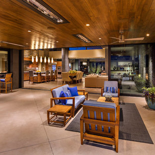 Foto di un grande patio o portico stile americano dietro casa con un caminetto, lastre di cemento e un tetto a sbalzo