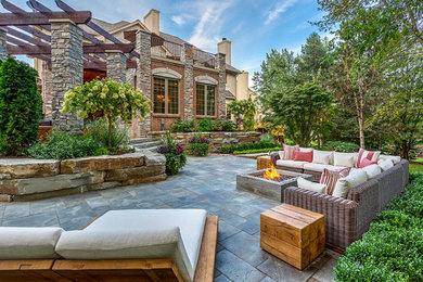 Inspiration for a large classic back patio in Orange County with a fire feature, natural stone paving and a pergola.