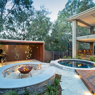 Large contemporary backyard patio in Melbourne with a fire feature and natural stone pavers.