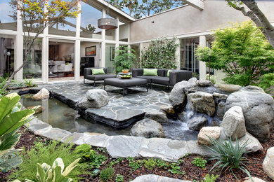 Inspiration for a large contemporary courtyard stone patio fountain remodel in Orange County with no cover