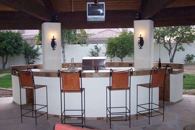 This is an example of a medium sized back patio in Phoenix with an outdoor kitchen, natural stone paving and no cover.