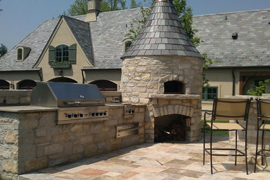 Example of a large classic backyard stone patio kitchen design in St Louis with no cover