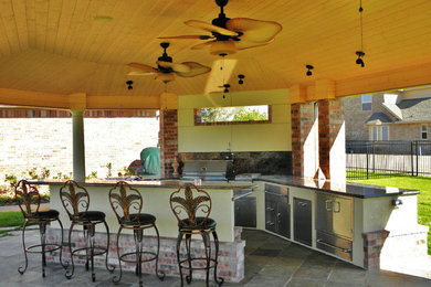 Patio kitchen - large traditional backyard stone patio kitchen idea in Houston with a roof extension