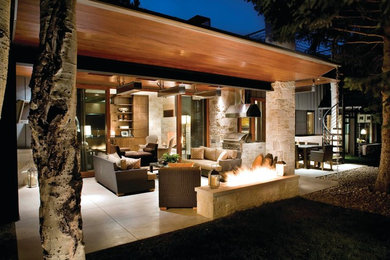 Aménagement d'une terrasse arrière contemporaine de taille moyenne avec un foyer extérieur, des pavés en pierre naturelle et une extension de toiture.