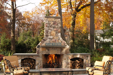 This is an example of a large classic back patio in New York with a fire feature, natural stone paving and no cover.