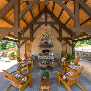Patio - large rustic backyard stone patio idea in Other with a roof extension and a fireplace