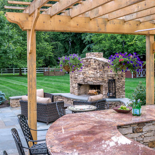 Ispirazione per un patio o portico country con un focolare, pavimentazioni in pietra naturale e una pergola