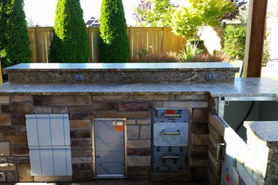 Example of a large classic backyard stone patio kitchen design in Portland with a pergola
