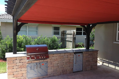 This is an example of a large contemporary back patio in Miami with an outdoor kitchen, brick paving and a pergola.