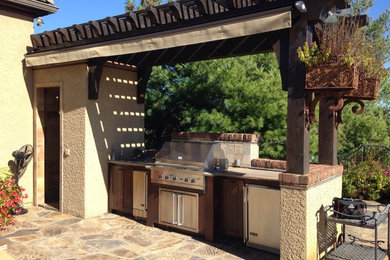 Imagen de patio clásico de tamaño medio en patio trasero con cocina exterior, adoquines de piedra natural y pérgola