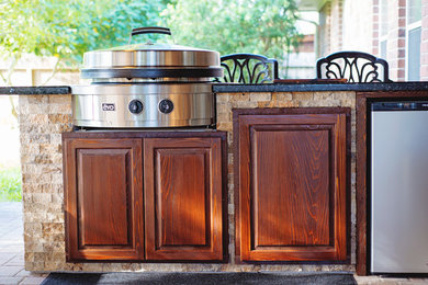 This is an example of a traditional back patio in Houston with an outdoor kitchen, brick paving and a roof extension.