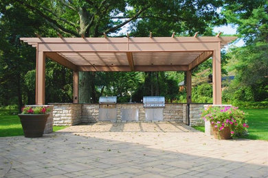 Modelo de patio clásico grande en patio trasero con adoquines de piedra natural, pérgola y cocina exterior