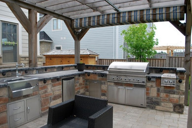 Imagen de patio tradicional de tamaño medio en patio trasero con cocina exterior, adoquines de ladrillo y pérgola