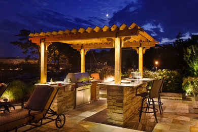 Modelo de patio clásico de tamaño medio en patio trasero con cocina exterior, adoquines de piedra natural y pérgola