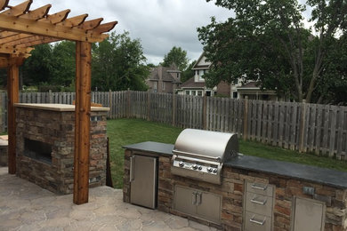 Large elegant backyard stone patio kitchen photo in Kansas City with a pergola