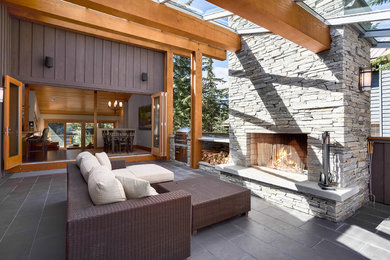 他の地域にある広いコンテンポラリースタイルのおしゃれな裏庭のテラス (タイル敷き、張り出し屋根、屋外暖炉) の写真