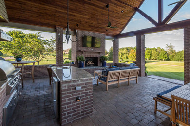 Cette image montre une grande terrasse arrière chalet avec une cuisine d'été, des pavés en béton et une extension de toiture.