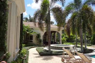 Diseño de patio tropical grande sin cubierta en patio trasero con fuente y adoquines de ladrillo