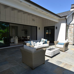 Foto di un patio o portico country di medie dimensioni e dietro casa con un focolare, pavimentazioni in pietra naturale e un tetto a sbalzo