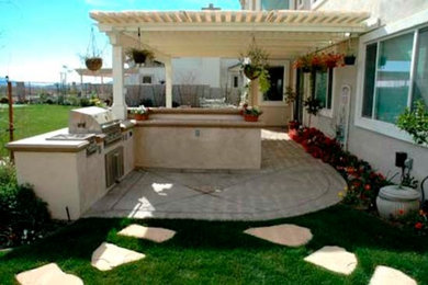 Patio kitchen - large backyard stone patio kitchen idea in Phoenix with a pergola