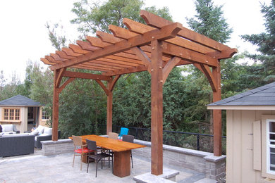 Medium sized rustic back patio in Toronto with natural stone paving and a pergola.