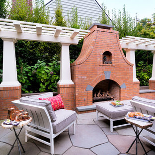Immagine di un patio o portico chic di medie dimensioni con pavimentazioni in pietra naturale, una pergola e un caminetto