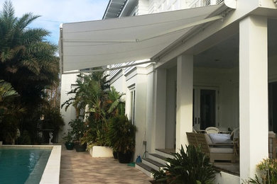 Mid-sized beach style backyard concrete paver patio photo in Jacksonville with an awning