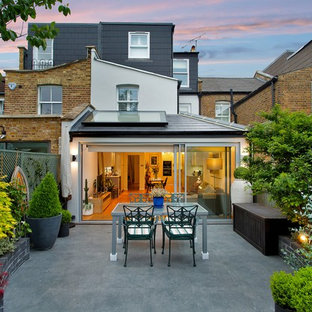 This is an example of a medium sized contemporary back patio in London with a potted garden, natural stone paving and no cover.