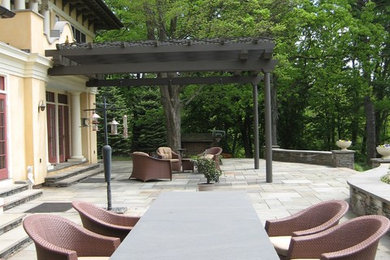 This is an example of an expansive back patio in New York with a potted garden, natural stone paving and a pergola.